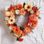 Orange flowers heart wreath featuring roses, chrysanthemums, gerberas, dahlias, alstromeria, greenery.