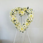 Heart-shaped floral arrangement on a stand against a white background