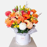 Orange toned flowers in a round white presentation box