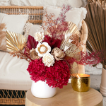 A mix of preserved flowers and silk flowers of hydrangea, Italian ruscus, silk flower, fox tail, palm arranged in a in white vase.