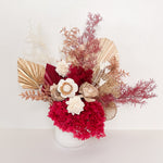 A mix of preserved flowers and silk flowers of hydrangea, Italian ruscus, silk flower, fox tail, palm arranged in a in white vase.