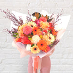 orange bouquet featuring orange and yellow tones of flowers - roses, dahlias, spray roses, snap dragon, lilies, gerberas & greenery.