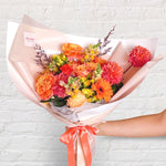 orange bouquet featuring orange and yellow tones of flowers - roses, dahlias, spray roses, snap dragon, lilies, gerberas & greenery.