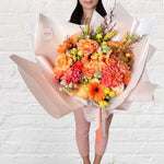 orange bouquet featuring orange and yellow tones of flowers - roses, dahlias, spray roses, snap dragon, lilies, gerberas & greenery.