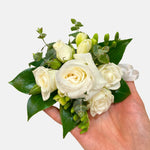 classic white corsage featuring roses, greenery, freesias, satin ribbon. Perfect for prom and weddings.