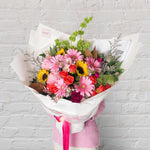 bright and vibrant seasonal bouquet with pink gerberas, sunflowers, orange roses, carnations and greenery