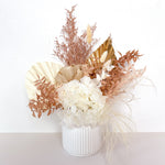 A mix of preserved flowers and silk flowers of hydrangea, misty, nigella, bunny tails, rice flower, baby’s breath, peony flower and palm in a in white vase.