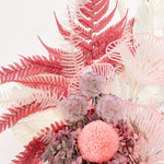 A mix of preserved flowers and silk flowers of hydrangea, ruscus, chrysanthemum, amaranthus, cloudy leaf, tiki grass, leather fern and scabiosa in a in white vase.