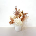 A mix of preserved flowers and silk flowers of hydrangea, misty, nigella, bunny tails, rice flower, baby’s breath, peony flower and palm in a in white vase.