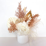 A mix of preserved flowers and silk flowers of hydrangea, misty, nigella, bunny tails, rice flower, baby’s breath, peony flower and palm in a in white vase.