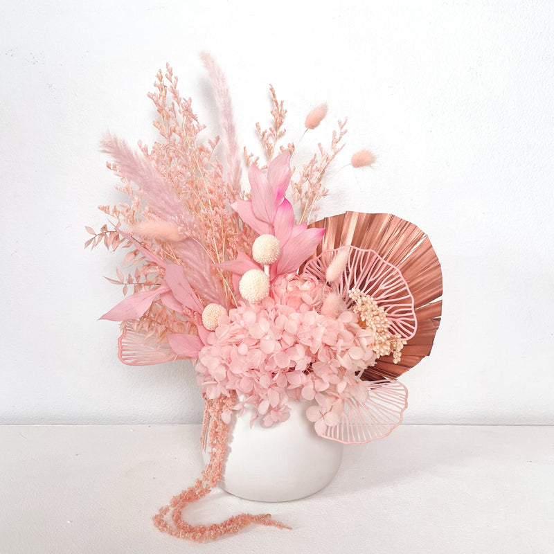 A mix of preserved flowers and silk flowers of hydrangea, ruscus, amaranthus, billy button, bunny tails, peony flower, rice flower, palm and fluffy stick in a in white vase.