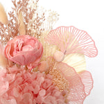 A mix of preserved flowers and silk flowers of hydrangea, Italian ruscus, bunny tails, baby's breath, rice flower, peony flower, palm and fluffy stick in a in white vase.